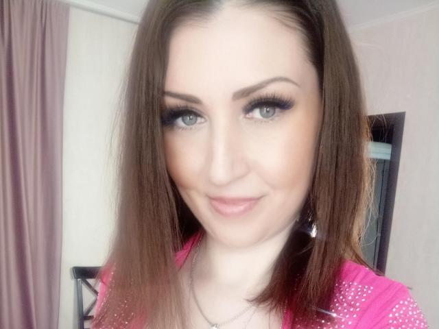 WikiStar has brown hair, blue eyes, and is wearing a pink top with white studs. She's smiling with a slight nose tilt and has thick black eyeliner.