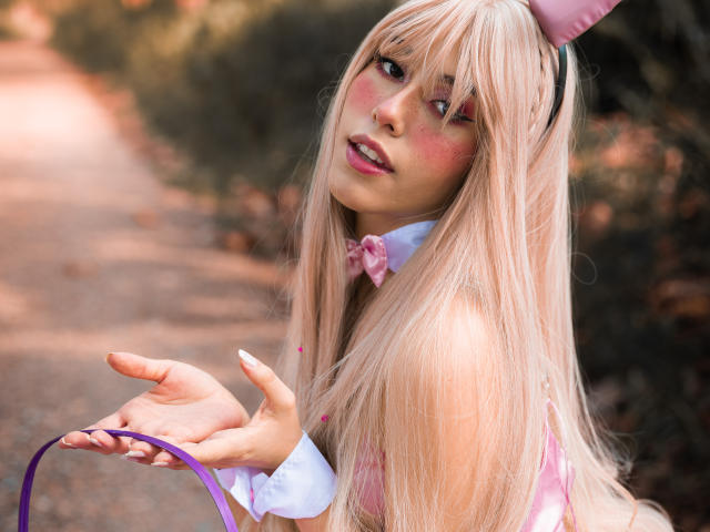ValerieBunny with long blonde hair, pink bunny ears, and a pink bowtie, holding a purple leash, looking back with pink cheeks, and slightly parted pink lips.