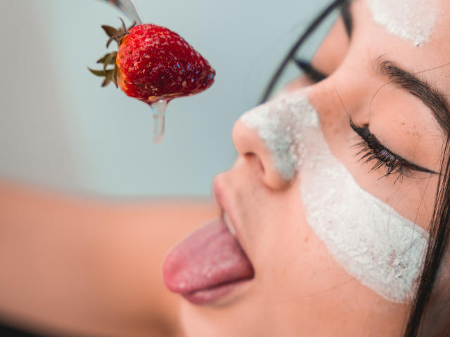 Le visage de ValerieBunny est recouvert d'une pâte blanche, sa langue est tirée, et elle regarde vers le haut une fraise rouge et dégoulinante tenue par une cuillère. Ses yeux sont fermés, et son maquillage est visible..