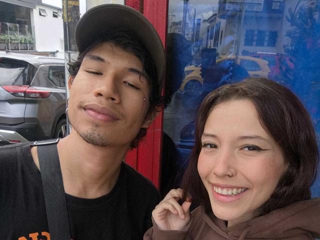 RoxanAndNoah, a cute Asian dude with a beard and hat, and a white chick with dark brown hair and eyeliner, smiling and taking a selfie together.