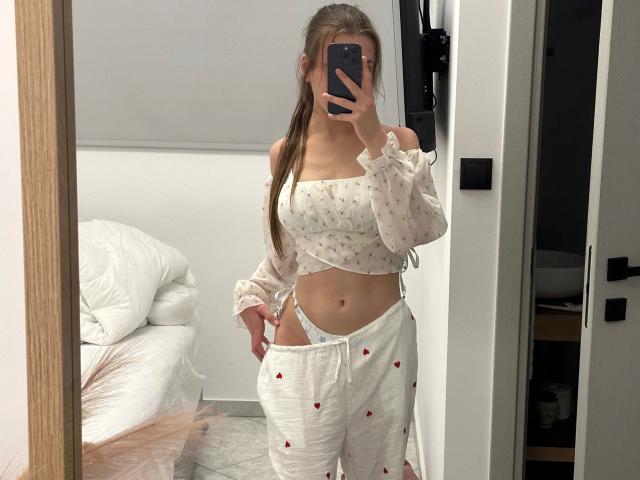 LunaLou-hot in white, off-shoulder, floral crop top, showing her small tits and white, strawberry-printed, loose pants with a visible, cute, tiny pussy, taking a mirror selfie.