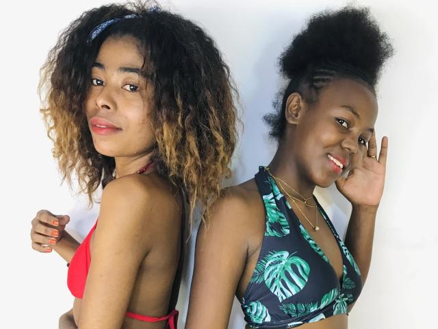 Silviesirene with curly brown hair, red bikini, and red lips, stands back-to-back with silviesirene, dark skin, green tropical bikini, and afro, showing a peace sign.