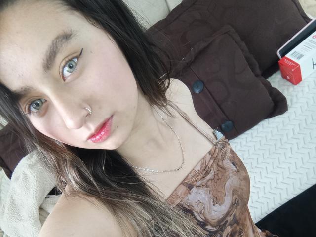 EymyFox ha la pelle chiara, gli occhi verdi e un piercing al naso, indossa una maglietta marrone a fantasia, ha i capelli lunghi marroni, il rossetto rosa e una collana d'argento..