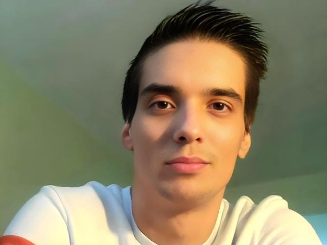 Steevident tiene un tono de piel medio, cabello corto y castaño oscuro, ojos marrones, y lleva una camisa blanca con mangas rojas. Está mirando a la cámara con una ligera sonrisa..