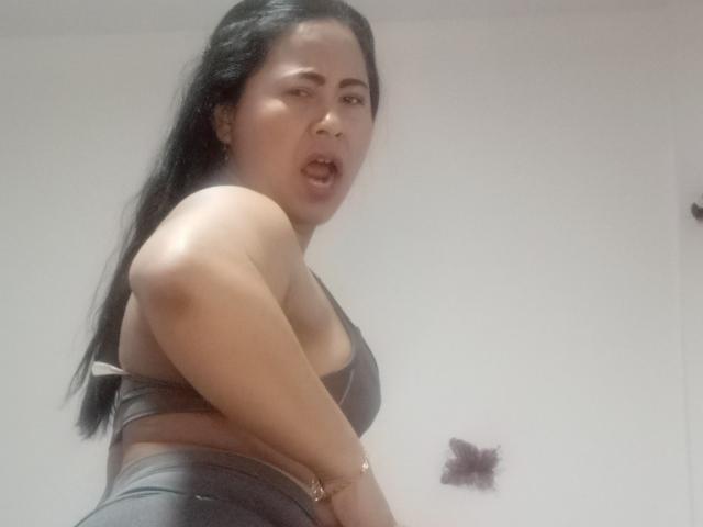 MiaSalomeChaude with long black hair, medium skin, wearing a black bra and leather pants, mouth slightly open, looking to the side, showing her small tits and slim ass.