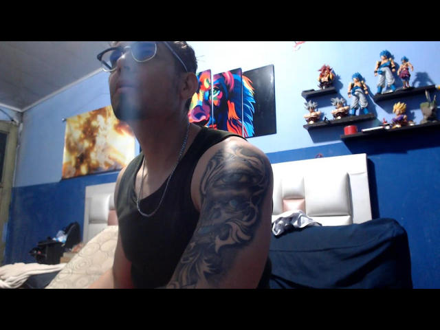 LeoAndKali with glasses, black tank top, and tattoo on right arm, looking up, in a blue-walled room with shelves of action figures and colorful artwork.