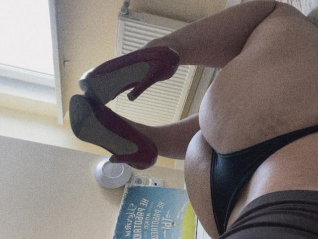Madrinia's thick thighs in red high heels with black thong, her curvy ass and soft belly, light skin, standing with legs crossed. Visible book and white ceiling fan.