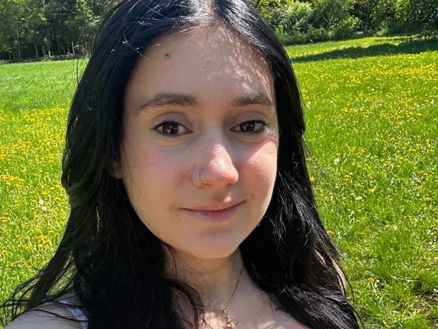 LenaLang-hot with black hair, brown eyes, nose ring, and subtle smile, standing in a sunny field with yellow flowers, showing her pretty face and cute ass.