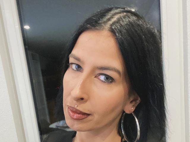 Candismimi-hot with black hair, blue eyes, hoop earrings, and a nose ring, slightly sticking out her tongue with glossy red lips.