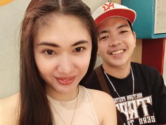 AsianCoupleDesire a de longs cheveux bruns et un visage mignon avec de petites seins, et elle porte un haut beige. AsianCoupleDesire se tient à côté d'un jeune homme asiatique souriant portant une casquette NY..