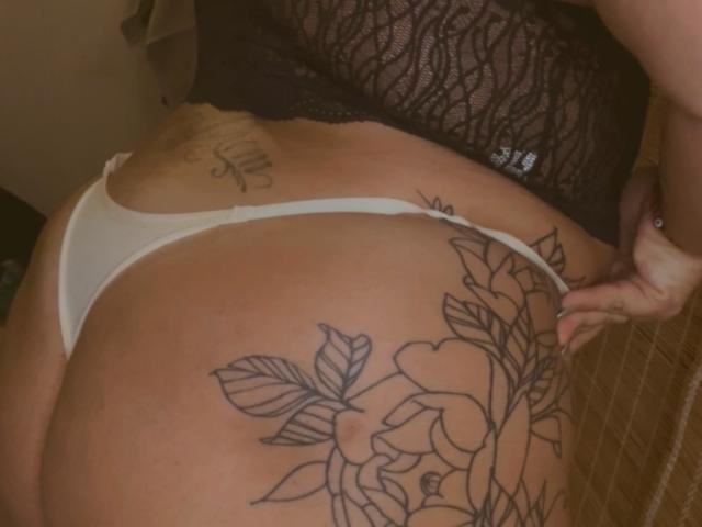 La biancheria intima bianca di ReinaMomoo, il suo sedere tatuato, una maglia di pizzo nero e un tatuaggio visibile sulla parte bassa della schiena. La sua mano è appoggiata sul fianco destro..