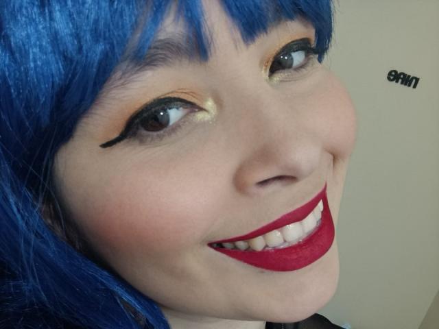 AgataP has blue hair, black eyeliner, shiny gold eyeshadow, and bright red lipstick, smiling with visible teeth. Her skin is light, and she's looking up slightly.