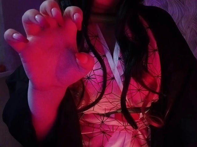 Rachel-Sweety-hot's foot up in the air, pinkish-red light on her skin, black hair, wearing a patterned pink and white kimono, black sleeves, toes painted white.