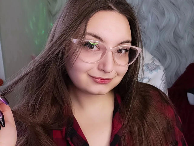 Rachel-Sweety-hot with long brown hair, wearing pink glasses, red plaid shirt, holding hair, smiling, pink lipstick, green reflection in glasses, slightly chubby, soft facial features.