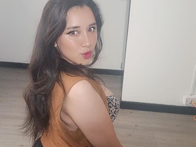 JessyBarnnett has long dark hair, wearing a sleeveless brown top with leopard print tits, looking over her shoulder with glossy pink lips and subtle makeup.