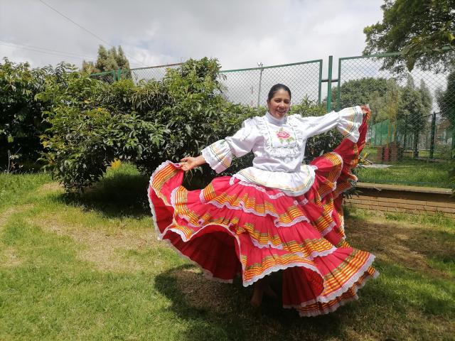PauletteLoveX, with dark hair, wearing a white blouse and red, yellow, and white striped, flared, ruffled skirt, stands in grass, holding skirt out, showing her ass.