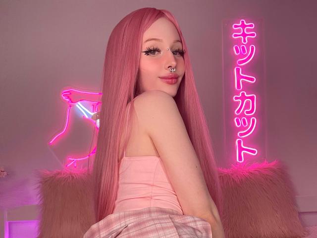 LaneyvilI tiene el pelo largo y rosa, un piercing en la nariz y lleva una camiseta rosa sin mangas con una falda escocesa. Letreros de neón rosados brillan detrás de ella, resaltando su aspecto lindo y sexy..