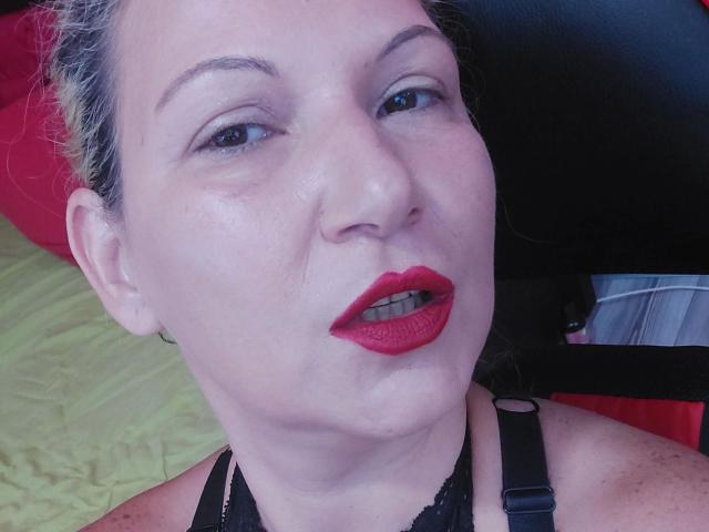 Lisabigtits-hot has pale skin, red lipstick, black eyeliner, and is wearing a black lace halter top with straps, looking up with slightly parted red lips.