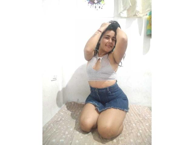 ScarletJamiesson is kneeling with hands in her long black hair, wearing a white crochet top and denim shorts, showing her small tits and cute ass.