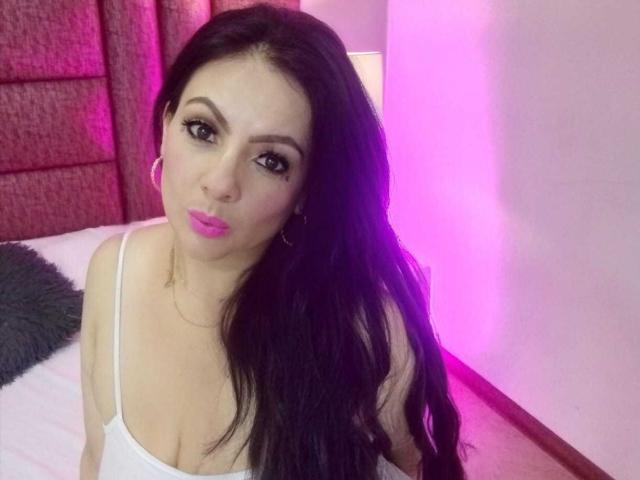 JakyKidman with long black hair, pink lipstick, hoop earrings, white spaghetti straps, looking at camera with pouty lips, pink and purple lighting, visible cleavage.
