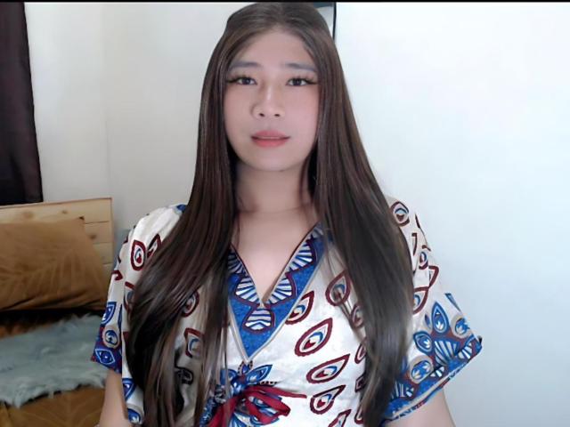 SophiaNicolex has long brown hair, wearing a white dress with blue and red patterns, looking at the camera with a slight smile, showing her boobs slightly in the dress.