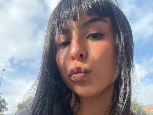 AdaWalton's pouty face with dark, straight hair, bangs, and brown eyes, making a slightly puckered, cute expression. She's got a small nose and a shiny, sunlit complexion.