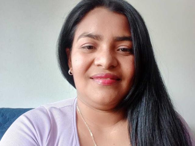CataleyaGomez has black straight hair, brown eyes, pink lipstick, and a slight smile. She wears a purple shirt and a silver necklace. Her ass is not visible.
