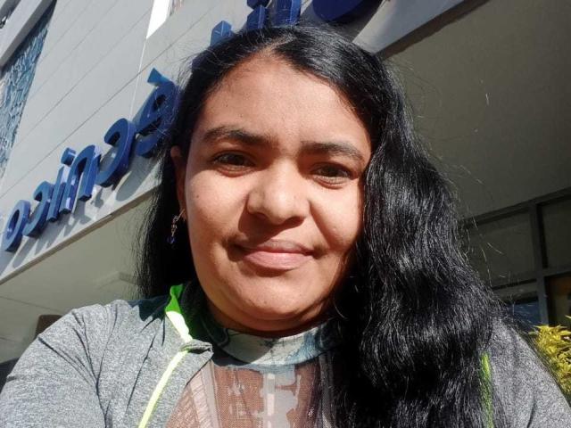 CataleyaGomez has a chubby face with dark brown skin, long black hair, and a subtle smile. She's wearing a gray hoodie with a green and white patterned scarf.