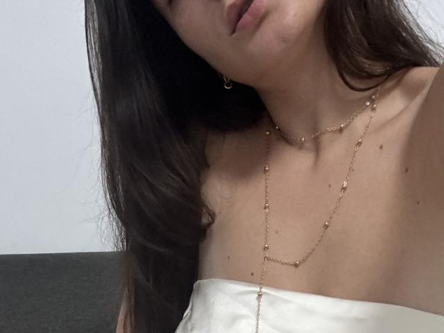EricaLust's face is partially visible, wearing a gold chain necklace, with long brown hair, white strapless top, and small earrings, showing her bare shoulders and chest.