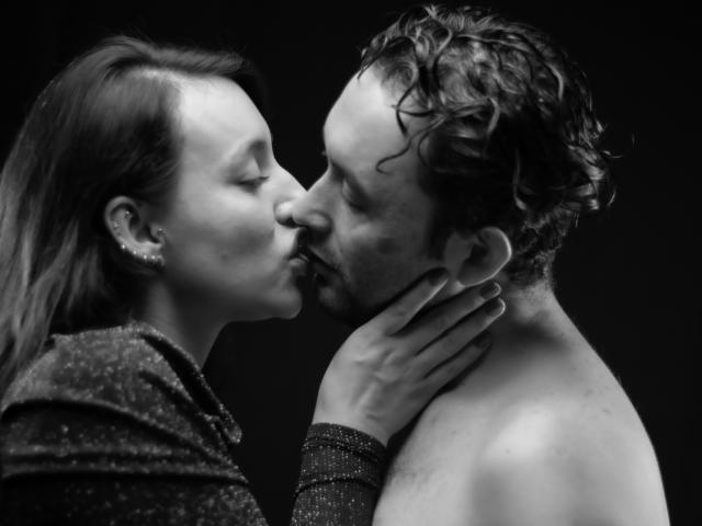 JeremmyAndStacy are kissing, her hand on his neck. She's wearing a sparkly top, he's shirtless with curly hair. Black-and-white photo, her nose touches his.