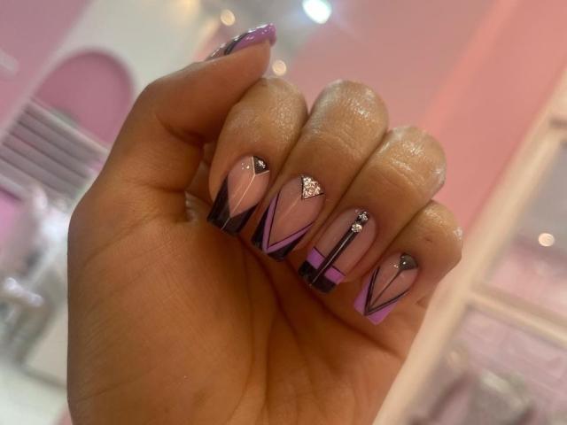 AlannaN's hand with shiny purple nails, black and pink geometric patterns, and silver rhinestones on the tips, showing off a cute and stylish manicure.