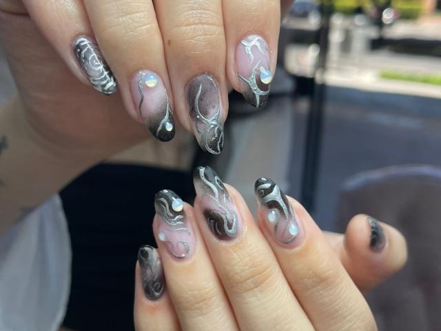 AlannaN's nails are super fly with glossy black and silver swirls on a pink base, featuring tiny rainbow gems on the tips. Her hands are looking hot.