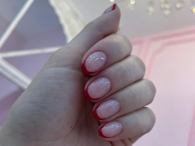 AlannaN's hand with shiny pink nails and red tips, showing off her neat, glossy fingernails. Her fingers are slightly curled, showcasing her well-maintained, pretty nails.