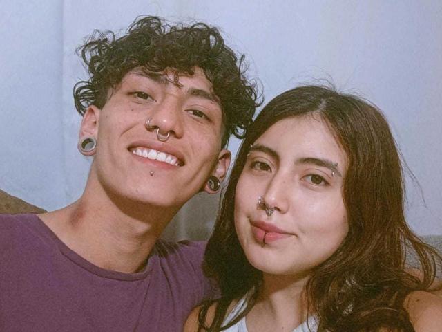 DainaAndMaik with curly black hair, nose rings, and ear plugs, smiling next to DainaAndMaik with long brown hair, nose rings, and lip ring, wearing a purple shirt.