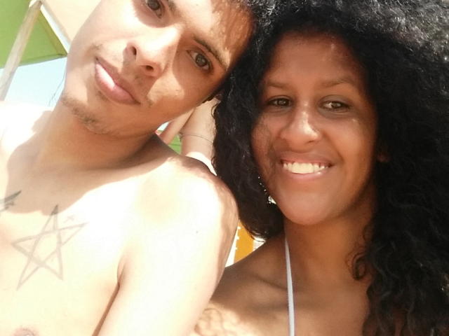 ShirliHot with curly black hair, smiling, has a cute face. ShirliHot's shirtless boyfriend has a star tattoo on his chest, brown hair, and a slight mustache.