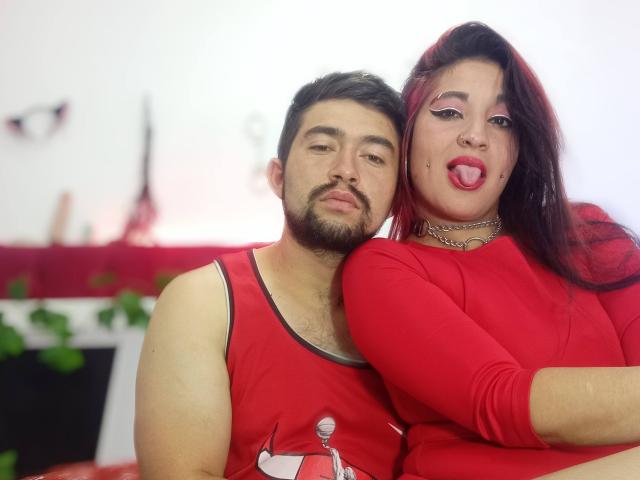 BonniClark with red hair, makeup, and lipstick, leans on a bearded man in a red tank top. Both wear red clothes, her arm around his shoulder, his eyes half-closed.