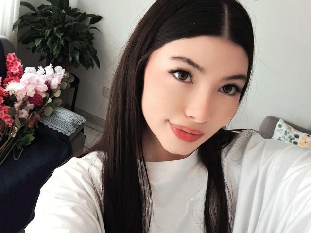 ViolettaLeroy has long black hair, fair skin, and red lips, wearing a white shirt, with a subtle smile, and a small nose ring, in a selfie.