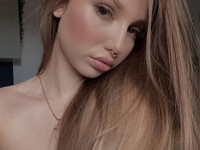 EmmaPassionate has long brown hair, a nose ring, and pinkish blush on her face. Her lips are slightly parted, showing a small amount of gloss. She's wearing a gold necklace.