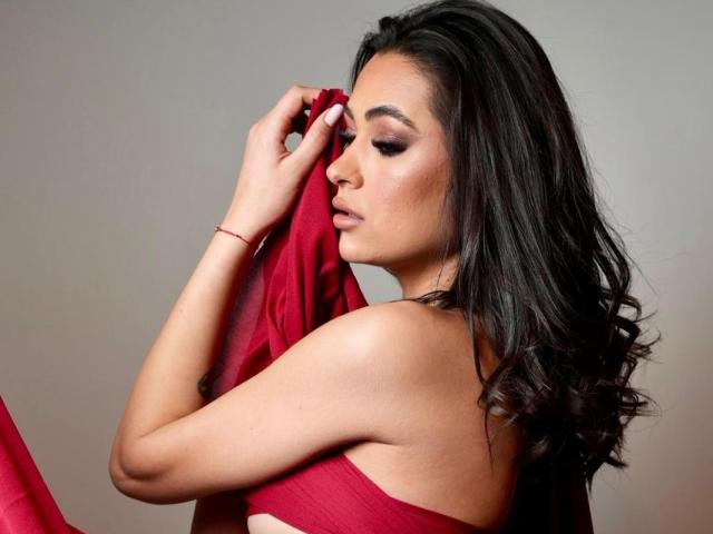 PrettyLiaa with dark, wavy hair holding a red cloth against her bare, sexy tits, eyes closed, wearing a red bracelet, soft light, elegant, sensual, confident.