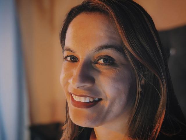 GabrielAndAbygail heeft bruin haar van gemiddelde lengte, een schattende glimlach met rode lippenstift, en bruine ogen. Haar huid is licht met een subtiele bruine tint. Ze kijkt naar de camera..