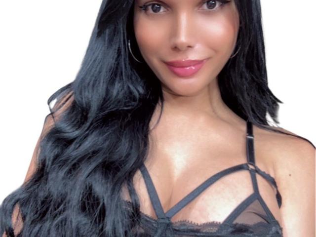 Vanezzatss with long black hair, red lipstick, hoop earrings, and a red bikini top, showing her tits and smiling slightly.