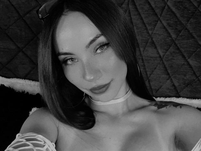 Black-and-white selfie of ValeryHarllow with long dark hair, hoop earrings, choker, and off-shoulder top, showing tits and a tattoo on the right shoulder. ValeryHarllow has a slight smile.