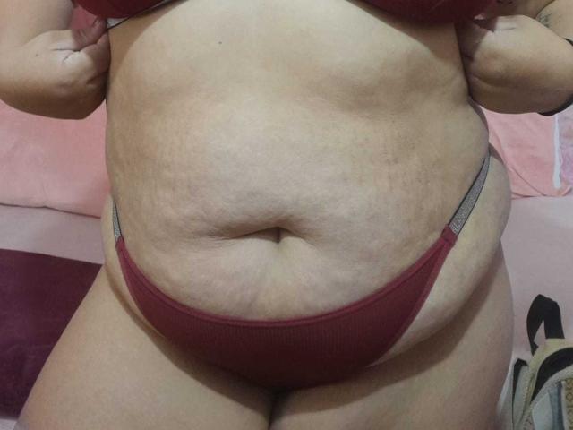 MelannieCarters dicker, blasser Bauch mit einigen Dehnungsstreifen, sie trägt rote Unterwäsche, ihre Hände liegen in der Nähe ihrer Brust und zeigen ein wenig ihrer großen, weichen und leicht hängenden Brüste..