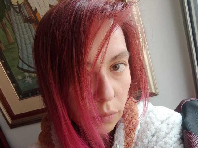 ArtemisFlyve with pink-dyed hair, pouty face, and brown eyes, wearing a fluffy white jacket, looking into the camera, nose ring visible.
