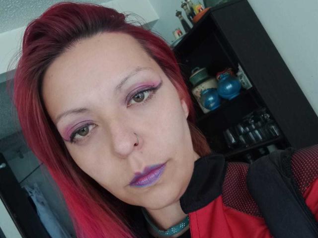 ArtemisFlyve heeft rood haar, paarse eyeliner, roze oogschaduw, paars lippenstift en een neusring. Ze draagt een rode en zwarte jas met een aanslag van gaas..