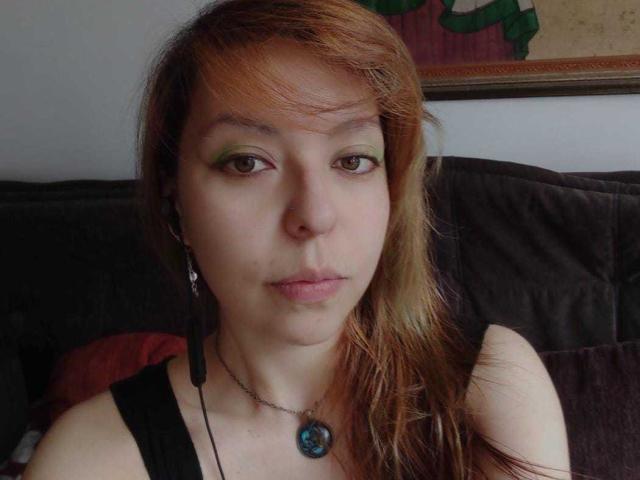 ArtemisFlyve ha la pelle chiara, il trucco agli occhi verde e i capelli marrone-rossastri. Indossa una canotta nera, una collana con una pietra blu e delle cuffie nere. È seduta su un divano scuro..