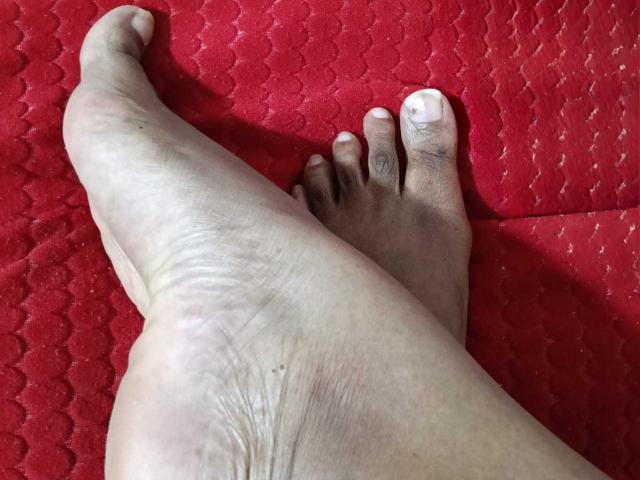 El pie y los dedos de EbonyAngelForU están sobre una alfombra roja con textura. Su planta está ligeramente arrugada y se puede ver la textura de la piel, y sus uñas de los pies son cortas y limpias..