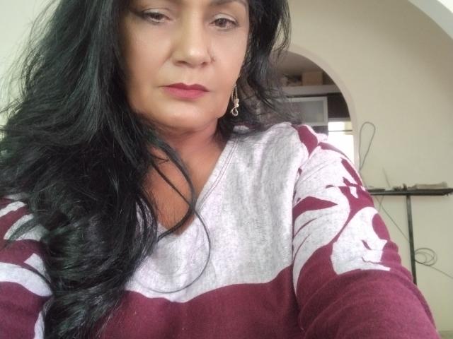 ZoeGuadalupe has long black hair, wearing a maroon and white sweater, with pink lipstick and earrings, looking slightly bored. Her tits are not visible.