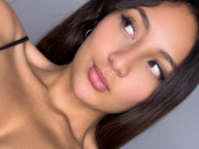 DianaFernandezz's face with closed eyes, slightly shiny lips, and a subtle smile, dark straight hair, and a small nose, resting her chin on her hand.