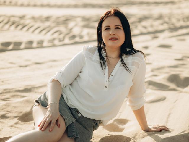 TayaBoret with dark hair, smiling, wearing a white button-up shirt, hands on shirt, sunlight, subtle makeup, soft expression, ring on left hand, bracelet on right wrist.